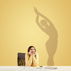 Image showing Young woman dreaming about future in big sport during her work in office. Becoming a legend. Shadow of dreams on the wall behind her. Copyspace.