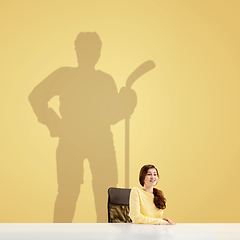 Image showing Young woman dreaming about future in big sport during her work in office. Becoming a legend. Shadow of dreams on the wall behind her. Copyspace.