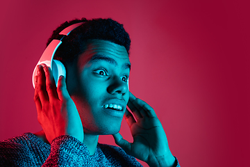 Image showing African-american man\'s portrait isolated on red studio background in multicolored neon light