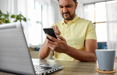 Image showing angry indian man with smartphone working at home