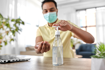 Image showing man in mask using hand sanitizer at home office