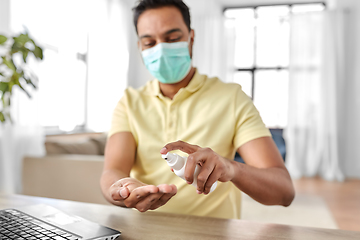 Image showing man in mask using hand sanitizer at home office