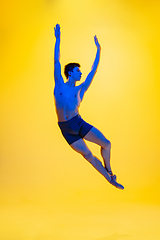 Image showing Young and graceful ballet dancer isolated on yellow studio background in neon light. Art, motion, action, flexibility, inspiration concept.