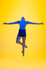 Image showing Young and graceful ballet dancer isolated on yellow studio background in neon light. Art, motion, action, flexibility, inspiration concept.