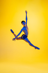 Image showing Young and graceful ballet dancer isolated on yellow studio background in neon light. Art, motion, action, flexibility, inspiration concept.