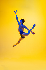 Image showing Young and graceful ballet dancer isolated on yellow studio background in neon light. Art, motion, action, flexibility, inspiration concept.