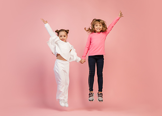 Image showing Happy kids, girls isolated on coral pink studio background. Look happy, cheerful, sincere. Copyspace. Childhood, education, emotions concept