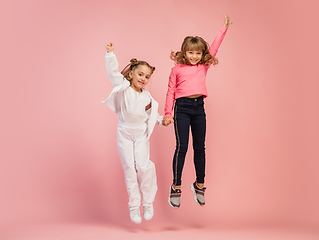 Image showing Happy kids, girls isolated on coral pink studio background. Look happy, cheerful, sincere. Copyspace. Childhood, education, emotions concept