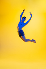 Image showing Young and graceful ballet dancer isolated on yellow studio background in neon light. Art, motion, action, flexibility, inspiration concept.