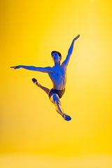 Image showing Young and graceful ballet dancer isolated on yellow studio background in neon light. Art, motion, action, flexibility, inspiration concept.