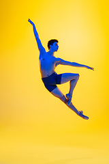 Image showing Young and graceful ballet dancer isolated on yellow studio background in neon light. Art, motion, action, flexibility, inspiration concept.