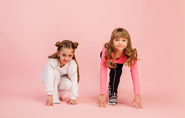 Image showing Happy kids, girls isolated on coral pink studio background. Look happy, cheerful, sincere. Copyspace. Childhood, education, emotions concept