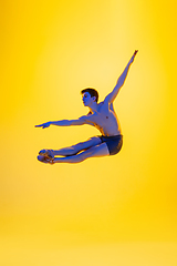 Image showing Young and graceful ballet dancer isolated on yellow studio background in neon light. Art, motion, action, flexibility, inspiration concept.