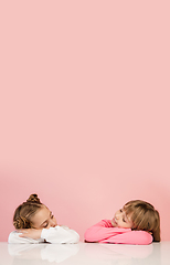 Image showing Happy kids, girls isolated on coral pink studio background. Look happy, cheerful, sincere. Copyspace. Childhood, education, emotions concept
