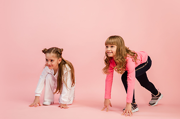 Image showing Happy kids, girls isolated on coral pink studio background. Look happy, cheerful, sincere. Copyspace. Childhood, education, emotions concept