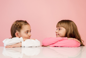 Image showing Happy kids, girls isolated on coral pink studio background. Look happy, cheerful, sincere. Copyspace. Childhood, education, emotions concept