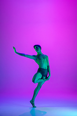 Image showing Young and graceful ballet dancer isolated on purple studio background in neon light. Art, motion, action, flexibility, inspiration concept.