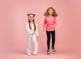 Image showing Happy kids, girls isolated on coral pink studio background. Look happy, cheerful, sincere. Copyspace. Childhood, education, emotions concept