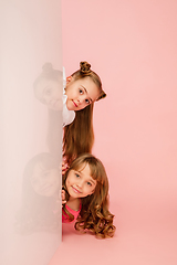 Image showing Happy kids, girls isolated on coral pink studio background. Look happy, cheerful, sincere. Copyspace. Childhood, education, emotions concept