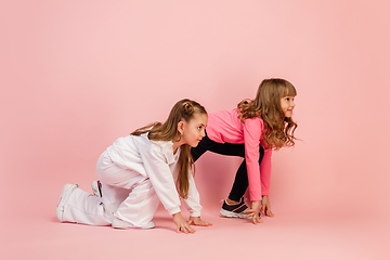 Image showing Happy kids, girls isolated on coral pink studio background. Look happy, cheerful, sincere. Copyspace. Childhood, education, emotions concept