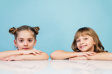 Image showing Happy kids, girls isolated on blue studio background. Look happy, cheerful, sincere. Copyspace. Childhood, education, emotions concept