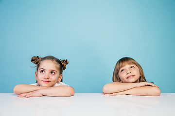 Image showing Happy kids, girls isolated on blue studio background. Look happy, cheerful, sincere. Copyspace. Childhood, education, emotions concept