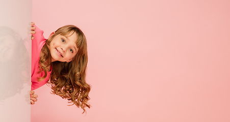 Image showing Happy kid, girl isolated on coral pink studio background. Looks happy, cheerful, sincere. Copyspace. Childhood, education, emotions concept