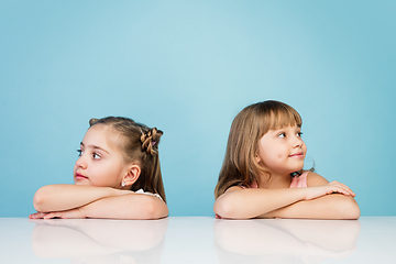 Image showing Happy kids, girls isolated on blue studio background. Look happy, cheerful, sincere. Copyspace. Childhood, education, emotions concept