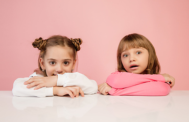 Image showing Happy kids, girls isolated on coral pink studio background. Look happy, cheerful, sincere. Copyspace. Childhood, education, emotions concept