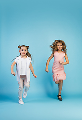 Image showing Happy kids, girls isolated on blue studio background. Look happy, cheerful, sincere. Copyspace. Childhood, education, emotions concept