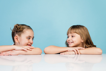 Image showing Happy kids, girls isolated on blue studio background. Look happy, cheerful, sincere. Copyspace. Childhood, education, emotions concept