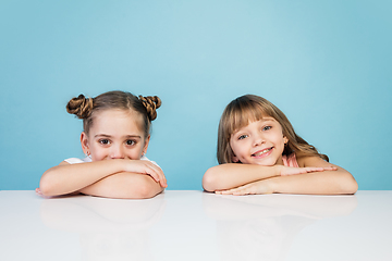 Image showing Happy kids, girls isolated on blue studio background. Look happy, cheerful, sincere. Copyspace. Childhood, education, emotions concept