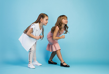 Image showing Happy kids, girls isolated on blue studio background. Look happy, cheerful, sincere. Copyspace. Childhood, education, emotions concept