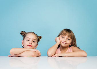 Image showing Happy kids, girls isolated on blue studio background. Look happy, cheerful, sincere. Copyspace. Childhood, education, emotions concept