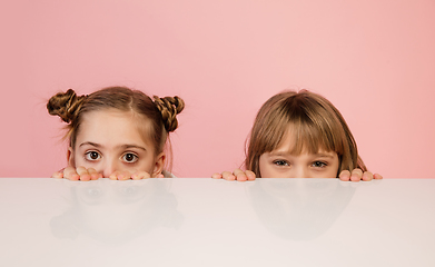 Image showing Happy kids, girls isolated on coral pink studio background. Look happy, cheerful, sincere. Copyspace. Childhood, education, emotions concept