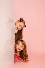 Image showing Happy kids, girls isolated on coral pink studio background. Look happy, cheerful, sincere. Copyspace. Childhood, education, emotions concept