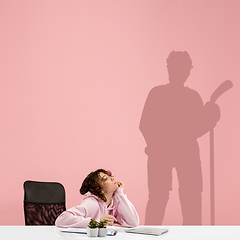 Image showing Young woman dreaming about future in big sport during her work in office. Becoming a legend. Shadow of dreams on the wall behind her. Copyspace.