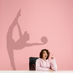 Image showing Young woman dreaming about future in big sport during her work in office. Becoming a legend. Shadow of dreams on the wall behind her. Copyspace.