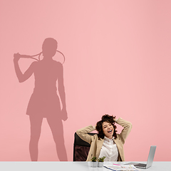 Image showing Young woman dreaming about future in big sport during her work in office. Becoming a legend. Shadow of dreams on the wall behind her. Copyspace.