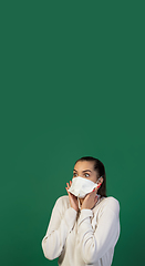 Image showing Woman in protective face mask isolated on green studio background. New rules of COVID spreading prevention