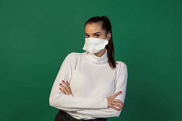 Image showing Woman in protective face mask isolated on green studio background. New rules of COVID spreading prevention