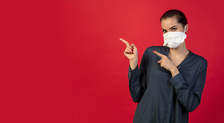 Image showing Woman in protective face mask isolated on red studio background. New rules of COVID spreading prevention