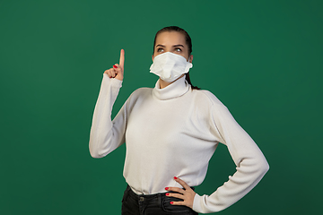 Image showing Woman in protective face mask isolated on green studio background. New rules of COVID spreading prevention