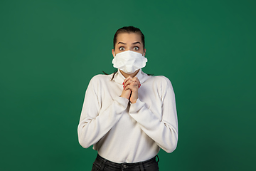 Image showing Woman in protective face mask isolated on green studio background. New rules of COVID spreading prevention