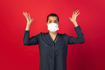 Image showing Woman in protective face mask isolated on red studio background. New rules of COVID spreading prevention