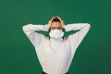 Image showing Woman in protective face mask isolated on green studio background. New rules of COVID spreading prevention