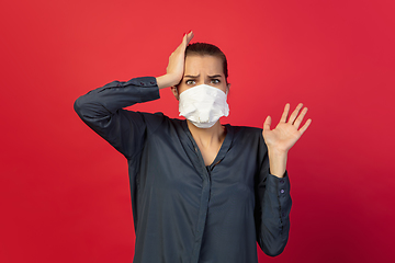 Image showing Woman in protective face mask isolated on red studio background. New rules of COVID spreading prevention