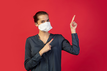 Image showing Woman in protective face mask isolated on red studio background. New rules of COVID spreading prevention