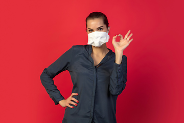 Image showing Woman in protective face mask isolated on red studio background. New rules of COVID spreading prevention