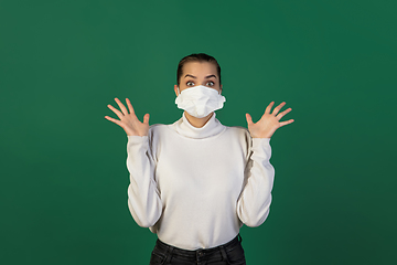 Image showing Woman in protective face mask isolated on green studio background. New rules of COVID spreading prevention